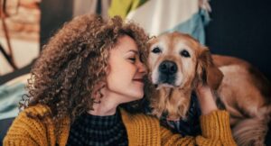 older golden retriever looking at camera while woman with curly hair cuddles into his face