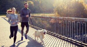 image of man and woman running with golden retriever dog on a lead