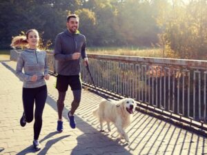 image of man and woman running with golden retriever dog on a lead