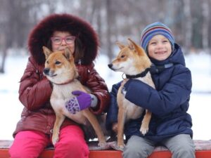 two children wearing big winter coats each cuddling a dog outside in the snow